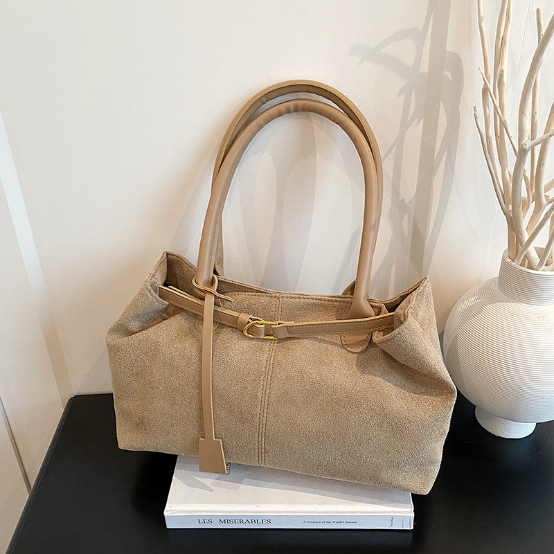 Beige handbag on a black surface with a white vase and books in the background