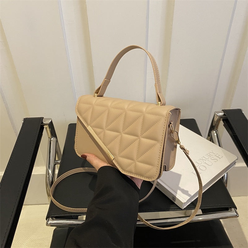 Beige quilted handbag held over a stack of books on a black surface.