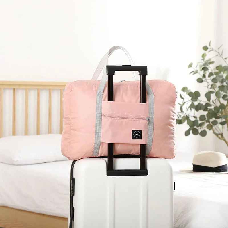 Pink foldable travel duffel bag with carry handles and front zip pocket.