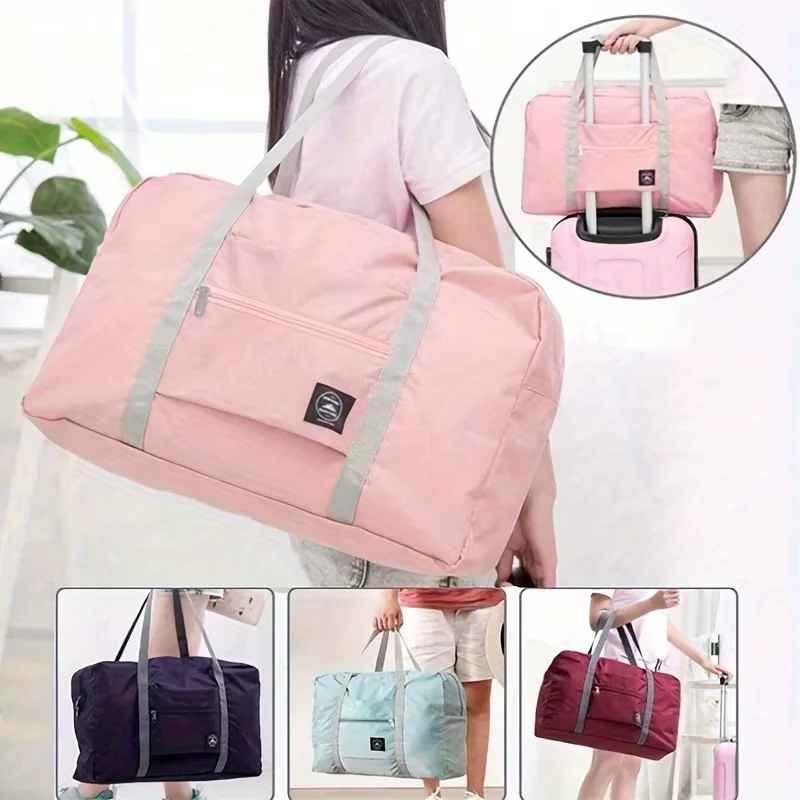 Pink foldable travel duffel bag with front zip pocket, dual carry handles, and trolley sleeve attached to a suitcase handle. Shown in pink, navy blue, blue, and red color options.