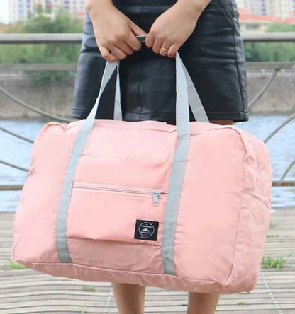 Pink foldable travel duffel bag carried by hand, showing large-capacity design.